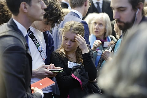 Swedish climate activist Greta Thunberg, center, watches a youth's phone inside the European Court of Human Rights, Tuesday, April 9, 2024 in Strasbourg, eastern France.