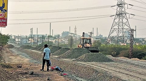An excavator levels a road near the under-construction bridge using stones 
