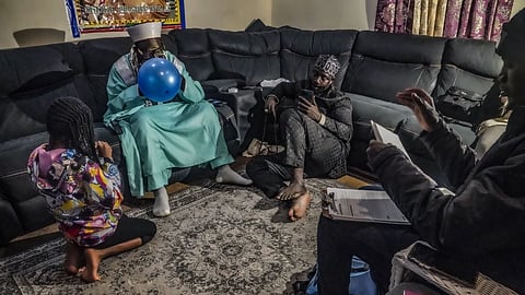 Imam Omar Niass, second from left, blows a balloon for his daughter Khadija, 8, while a migrant from Senegal completes documents for a city identification at Bronx's Masjid Ansaru-Deen mosque, Friday, March 15, 2024, in New York. 