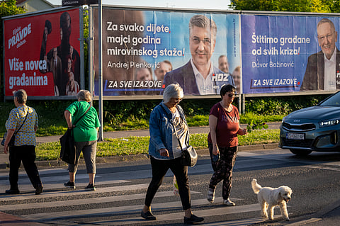 Pedestrians cross a street in front of election posters in Zagreb, Croatia, Sunday, April 14, 2024. 