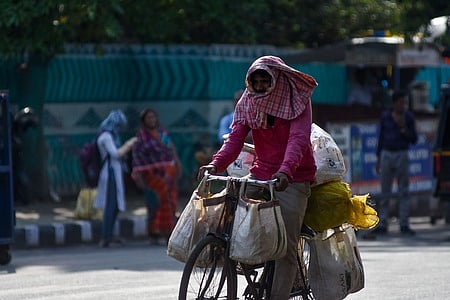 A man riding a cycle cover his head with a towel from heat.