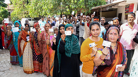 People show their identity cards as they wait in queues to cast their vote at a polling station, during the sixth phase voting for Lok Sabha elections, in Prayagraj on Saturday.