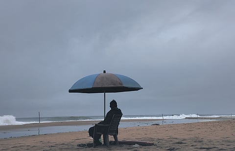 A lifeguard at Papanasam Beach in Varkala looks on at an overcast sky 