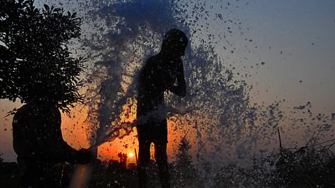 Children bathe from a pipe on a hot summer day amid heatwave.