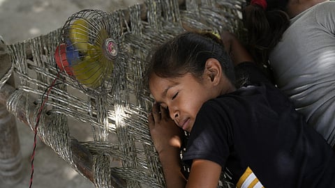 A child rests near a portable fan on a hot summer day amid heatwave, in New Delhi.