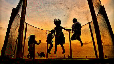 Children jump on a trampoline on the backdrop of sunset as they enjoy their summer vacations, at Bhuigaon Beach in Mumbai.
