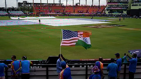 A fan waves a flag as the pitch area is seen covered after wet outfield delayed the toss for the ICC Men's T20 World Cup second semifinal cricket match between England and India at the Guyana National Stadium in Providence, Guyana.
