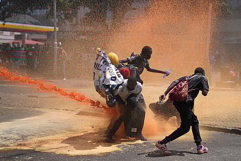 Protesters hide behind a banner as police fire tear gas at them during a protest over proposed tax hikes in a finance bill in downtown Nairobi, Kenya Tuesday.