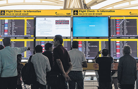 Passengers look at screens, some of them showing Blue Screen errors, at T3 of Delhi International Airport on Friday.