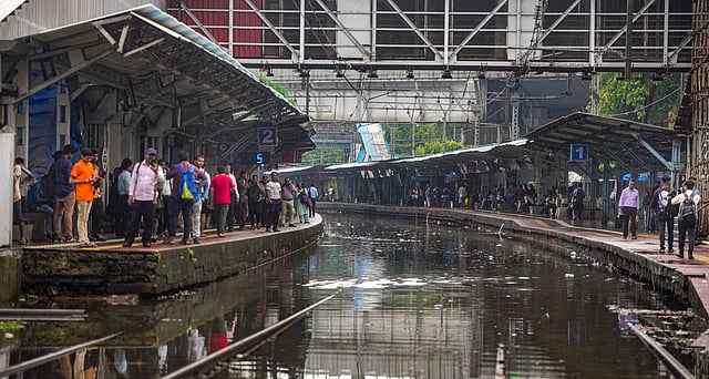Passengers wait for trains at a waterlogged railway station, during rains, in Mumbai, Monday.
