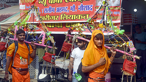 Kanwariyas walk past a shop on which banners with shopkeeper's name was put up on Kanwar Marg after an order issued by Uttar Pradesh Government, in Muzaffarnagar, Saturday, July 20, 2024. 