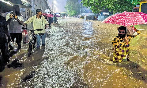 People wade through the flooded service road of NH-16 near Iskcon temple