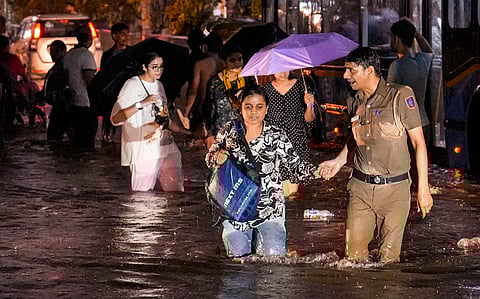 A woman being assisted by a police official while wading through a waterlogged road during rain near Old Rajinder Nagar area, in New Delhi, Wednesday, July 31, 2024.