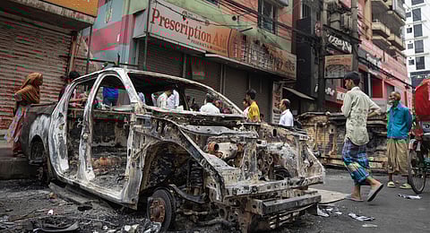 People walk past a vandalised car in Dhaka, Bangladesh, Tuesday, Aug. 6, 2024. 