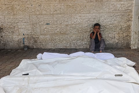 A child sits beside the shrouded corpses of people killed in an overnight Israeli strike, in the yard of the Al-Aqsa Martyrs hospital in Deir el-Balah in the central Gaza Strip on August 10, 2024.