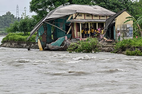 Students and villagers stand outside a partially collapsed government school following severe soil erosion after an increase in the water level of the Sermanga river during monsoon season in the New Banglajhora village of Kokrajhar district in Assam on August 10, 2024.
