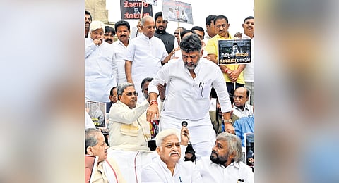 Chief Minister Siddaramaiah lends a hand to Deputy Chief Minister DK Shivakumar, as he stands up to address a gathering of Congress leaders, at a protest against Governor Thaawarchand Gehlot in Bengaluru on Saturday 