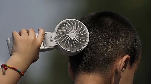A boy cools himself with an electric fan on a sweltering day at a park in Tongzhou, on the outskirts of Beijing.