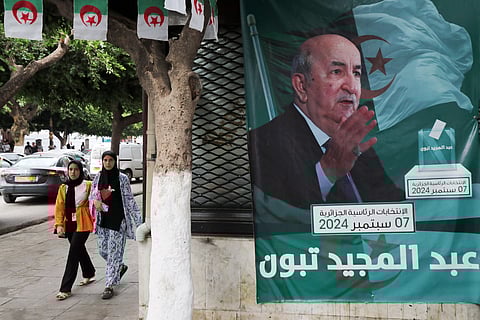 People walk past posters of Algeria's President Abdelmajid Tebboune outside an election campaign headquarters in Algiers on September 8, 2024. 