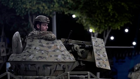 A Lebanese army soldier sits behind his weapon on the top of an armored personnel carrier at the site of an Israeli airstrike in Beirut's southern suburb, Monday, Sept. 23, 2024.