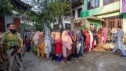 A security official stands guard as voters wait in a queue at a polling station to cast votes during the second phase of Jammu and Kashmir Assembly elections, in Srinagar.