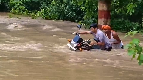 Commuters wade through a flooded area after an increase in the water level of Gandak river due to heavy rainfall, in Bagaha, Bihar.
