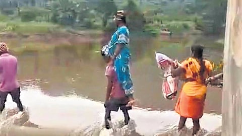 Carrying Jyothi on his shoulders, her husband crosses the swollen Jaderu canal near Pinjari Konda in the Alluri Sitarama Raju district 