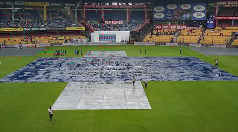 Groundsmen cover the pitch area as it rains on the first day of the first cricket test match between India and New Zealand at M Chinnaswamy Stadium, in Bengaluru. 