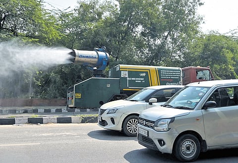 Commuters ride past an anti-smog gun spraying water