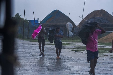 People brave through gusting wind as they walk near Dhamara fishing harbour ahead of cyclone Dana's landfall in Bhadrak district.