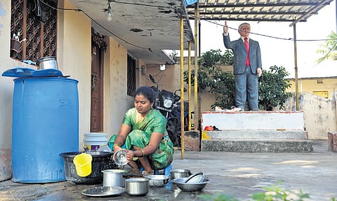 A woman washes vessels in front of the statue of Donald Trump installed by Bussa Krishna at his house in Konne village, Jangaon district 