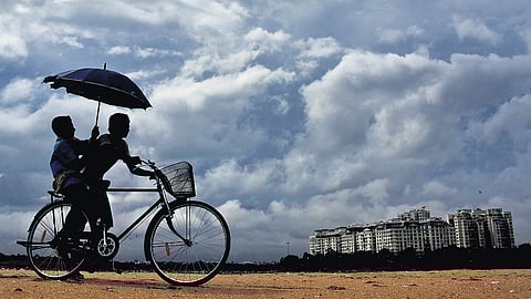 Kids share an umbrella as they ride through Srinivasapuram, Chennai, under a clouded sky on Monday
