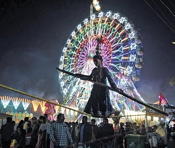 A girl walks the tightrope while the Ferris wheel rolls in the background at Balijatra.