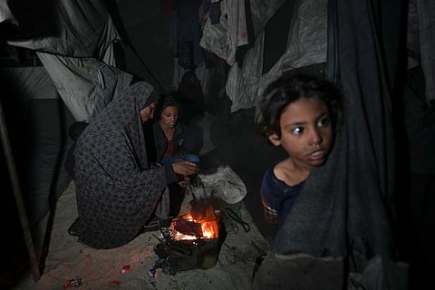 Shireen Daifallah, who was displaced with her children from northern Gaza, checks the fire next to their tent at a camp for displaced people in Deir al-Balah. Gaza Strip.