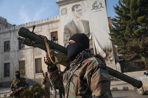 A Syrian opposition fighter holds a rocket launcher in front of the provincial government office, where an image of Syrian President Bashar Assad is riddled with bullets on the facade, in the aftermath of the opposition's takeover of Hama, Syria, Friday, Dec. 6, 2024.