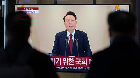 People watch a TV screen showing the live broadcast of South Korean President Yoon Suk Yeol's announcement at the Seoul Railway Station in Seoul, South Korea.