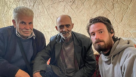 In this photo provided by the Syrian Emergency Task Force, American Travis Timmerman, right, sits with Mosaed al-Rifai, center, who found him in the Syrian desert, and the owner of the house where he took refuge, left, name not available, in Damascus, Syria on Thursday Dec. 12, 2024. 