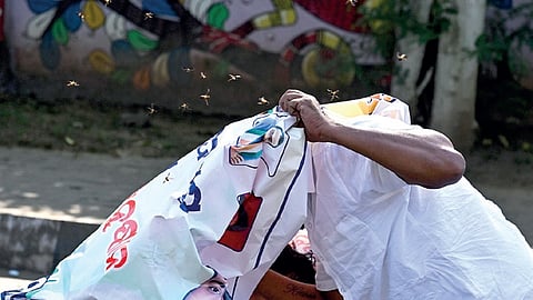 A protester takes cover under a banner as bees swarm the protest site of Youth Congress workers at Forest Park, in Bhubaneswar on Monday.