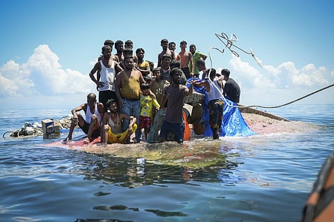 Ethnic Rohingya refugees stand on their capsized boat as rescuers throw a rope to them off West Aceh, Indonesia, on March 21, 2024.