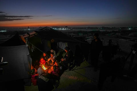 Reda Abu Zarada, 50, displaced from Jabaliya in nothern Gaza, sits by a fire with her grandchildren at a camp by the sea in Khan Younis, Gaza Strip.