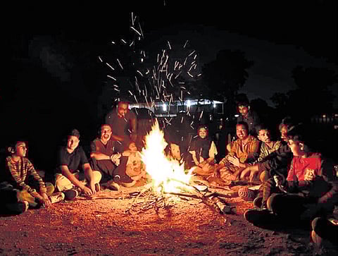 People sit around a bonfire during a night camp at Forest Trek Park, Chilkur, organised by TGFDC 