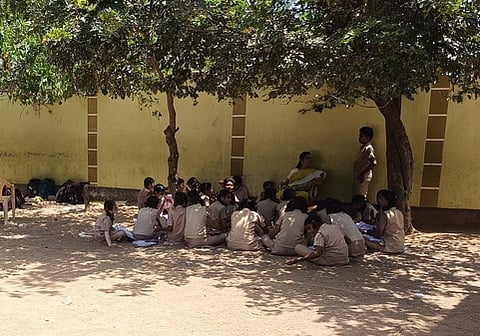 Portion of students of Muthaliyarpatti Government Higher Secondary School near Kadayam are forced to study under trees, sitting on the ground due t