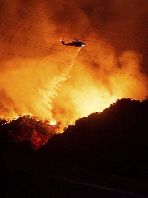 Firefighters watch as water is dropped on the Palisades Fire in Mandeville Canyon Saturday, Jan. 11, 2025, in Los Angeles.