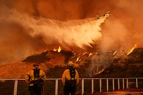 A resident sprays their property with a garden hose as the Eaton Fire engulfs structures across the street, Wednesday, Jan. 8, 2025, in Altadena, California.