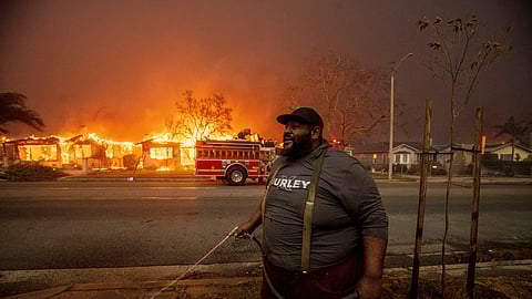 A resident sprays their property with a garden hose as the Eaton Fire engulfs structures across the street, Wednesday, Jan. 8, 2025, in Altadena, California.