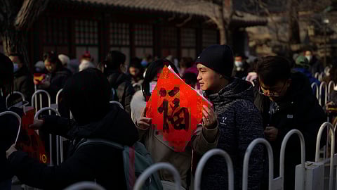 A woman holds a red paper with Chinese calligraphy "Good Fortune" as people line up to get the red paper distributed by Baiyun Taoist Temple ahead of the Lunar New Year in Beijing, Wednesday, Jan. 22, 2025. 