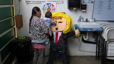 A migrant woman from the Mexican state of Guerrero holds her 1-year-old granddaughter as she hits a piñata of President Donald Trump at a shelter for migrants Wednesday, Jan. 22, 2025, in the border city of Tijuana, Mexico. 