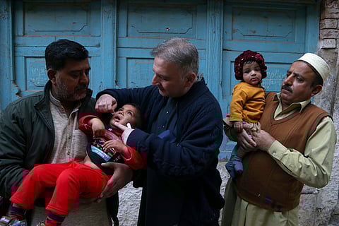 A health worker, center, administers a polio vaccine to a child at a neighbourhood in Peshawar, Pakistan on Monday.