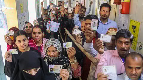 Voters show their ID cards as they wait in queues at a polling booth to cast votes during the Delhi Assembly elections, at Shahzada Bagh in New Delhi.