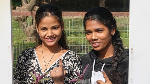 Voters show their fingers marked with indelible ink and plant saplings received from the polling officials as they pose for photographs after casting vote at a polling station during the Delhi Assembly elections, in New Delhi.